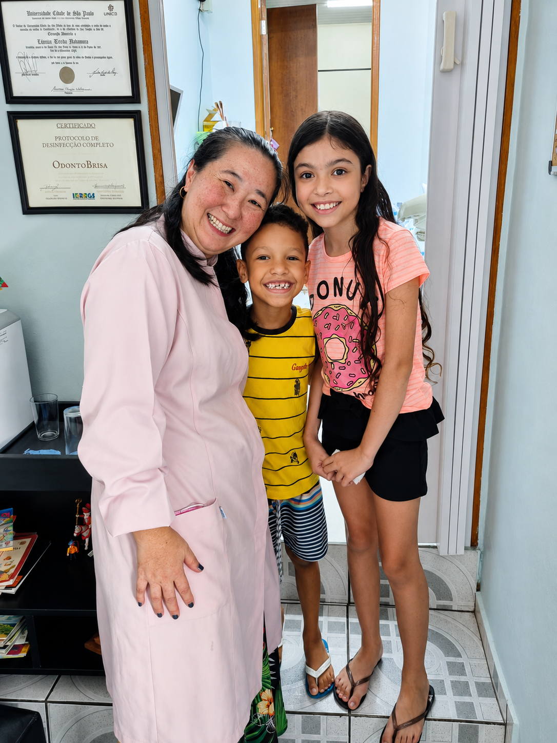 Profissional da OdontoBrisa sorrindo ao lado de duas crianças no consultório